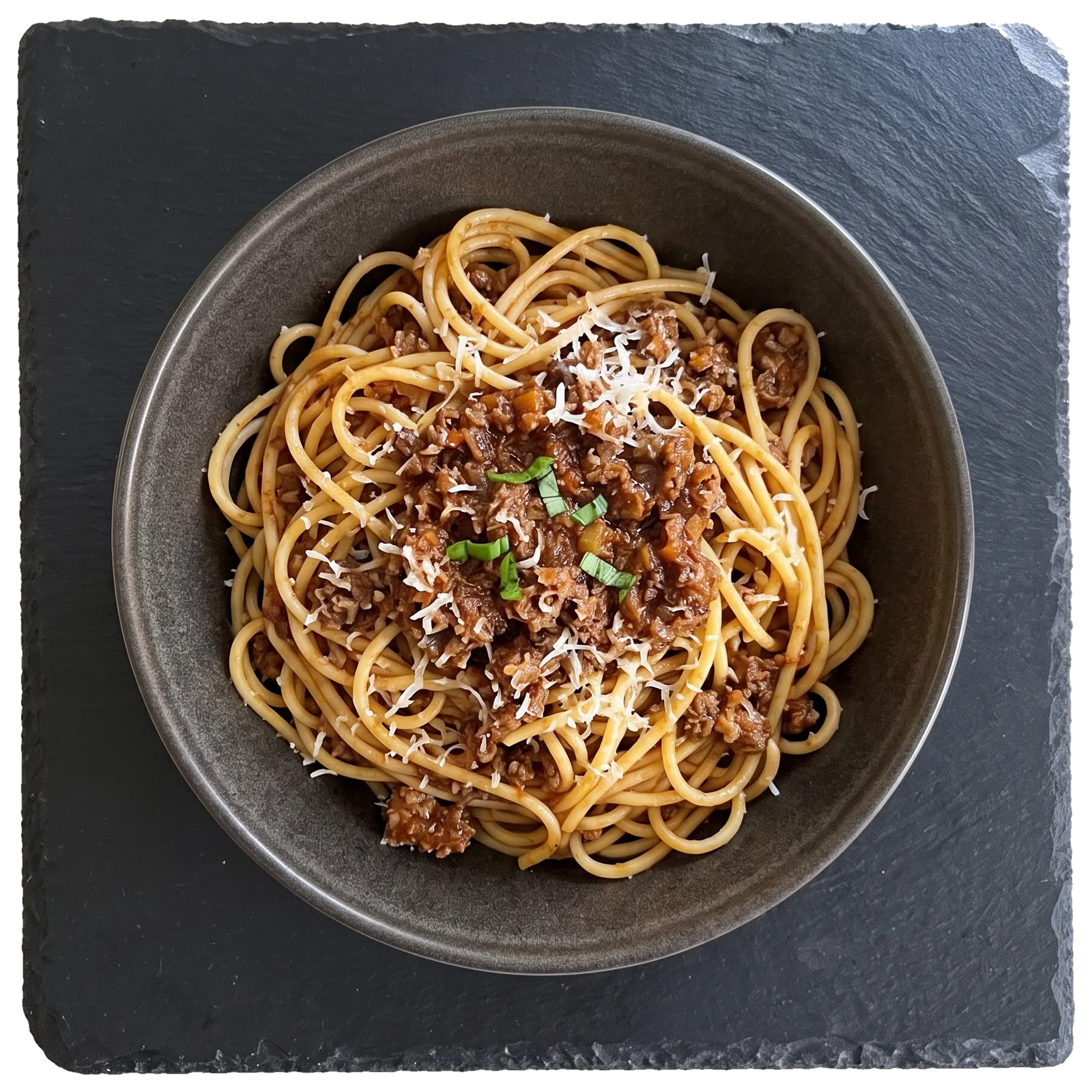 Spaghetti Bolognese mit geriebenem Käse in einer dunklen Schale auf einer Schieferplatte