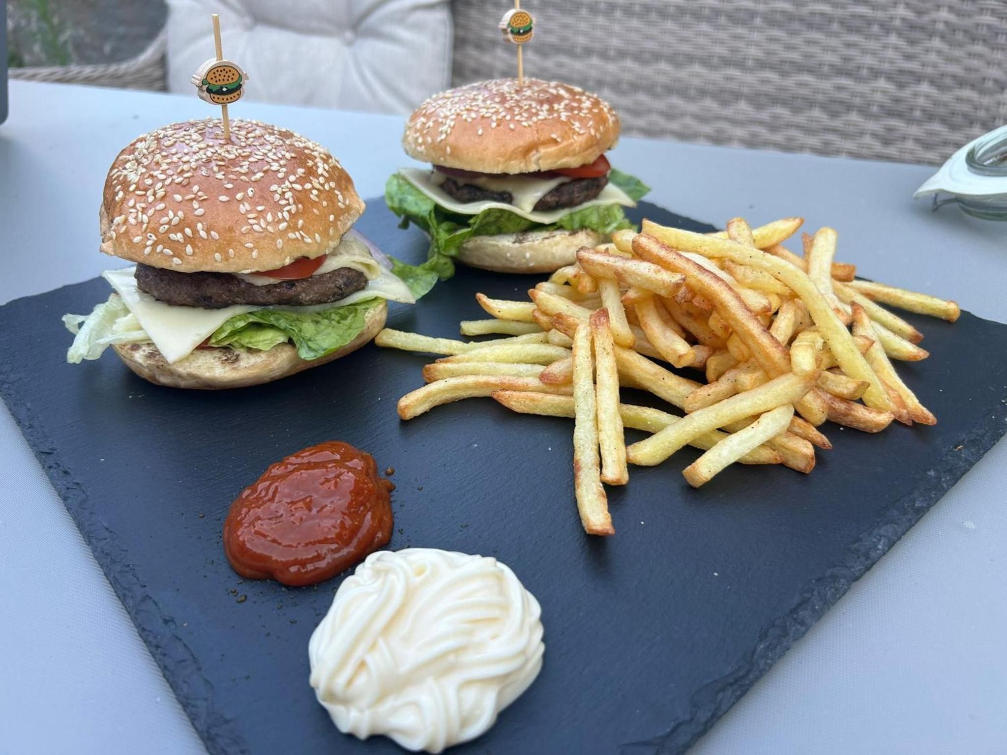 Abendessen: zwei Cheeseburger mit Pommes, Ketchup und Mayonnaise auf einer Schieferplatte