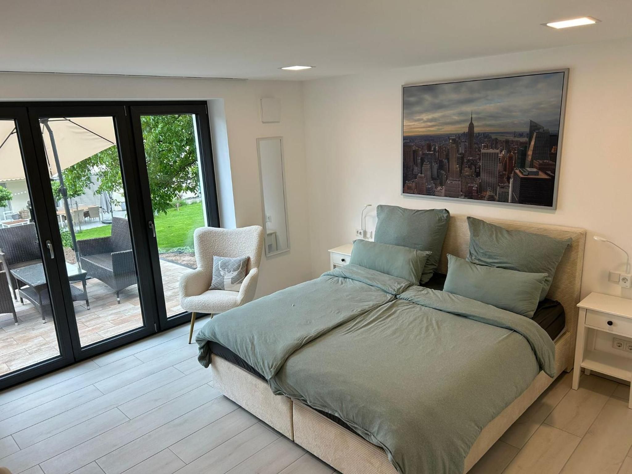 Doppelzimmer: Doppelbett mit Nachttischen unter einem Wandbild von New York, links Sessel und Terrassentür