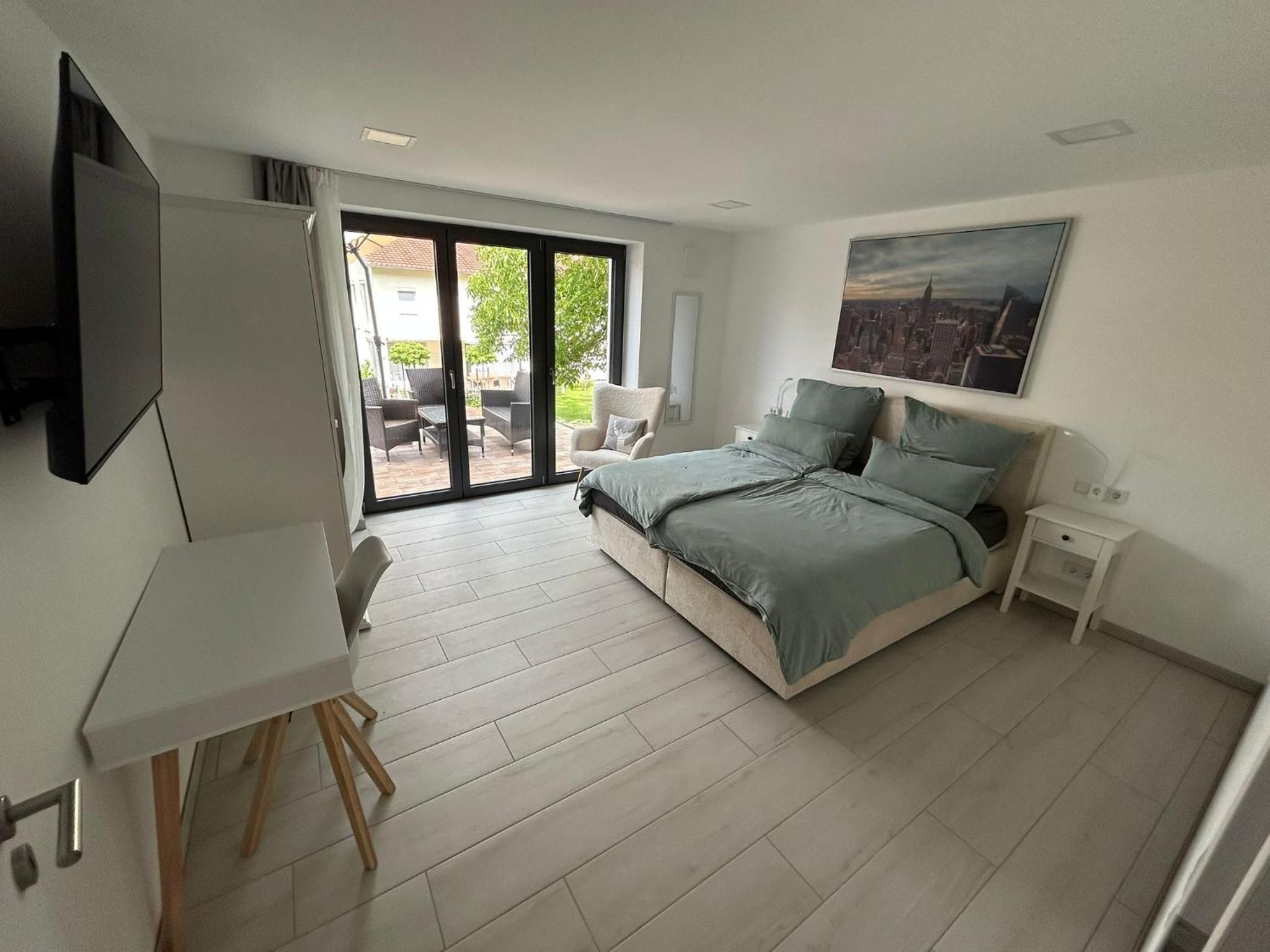 Doppelzimmer von der Tür aus: Schreibtisch, Fernseher, Bett mit Nachttischen und Terrassentür