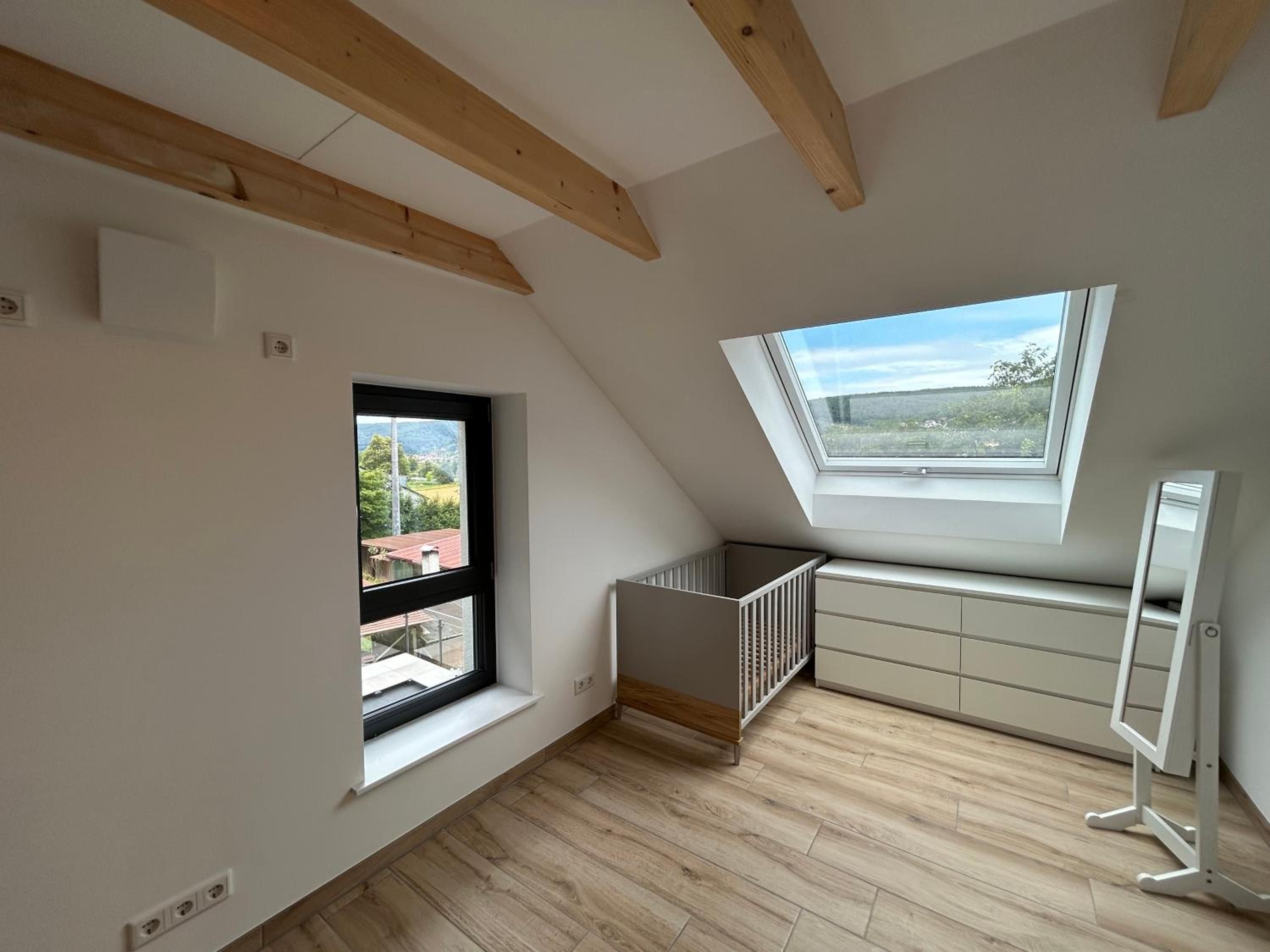Schlafbereich im Apartment mit Kinderbett, Kommode und Dachfenster