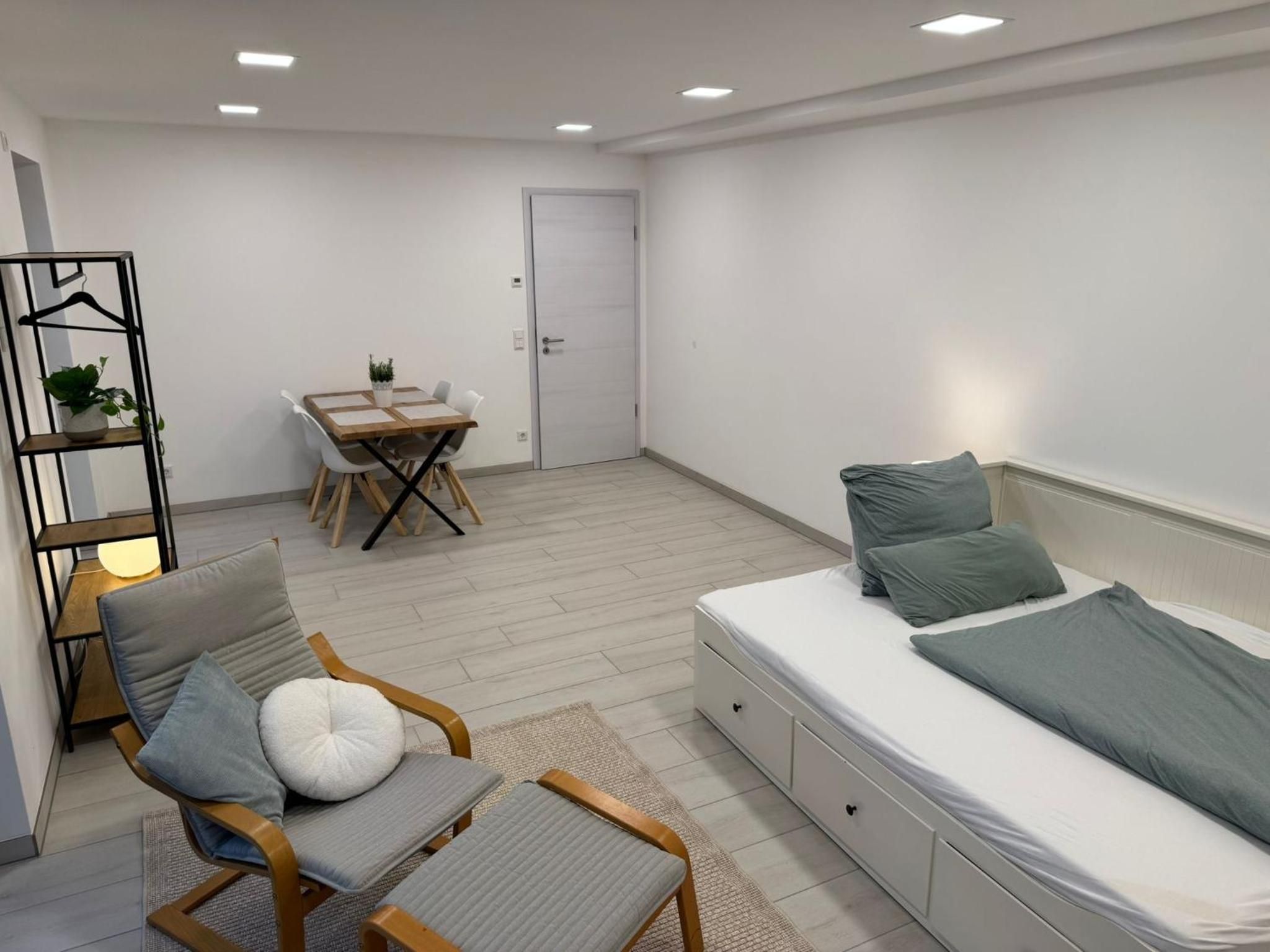 Wohnzimmer: Tagesbett als Bett bezogen, Relaxsessel mit Hocker, dahinter der Esstisch