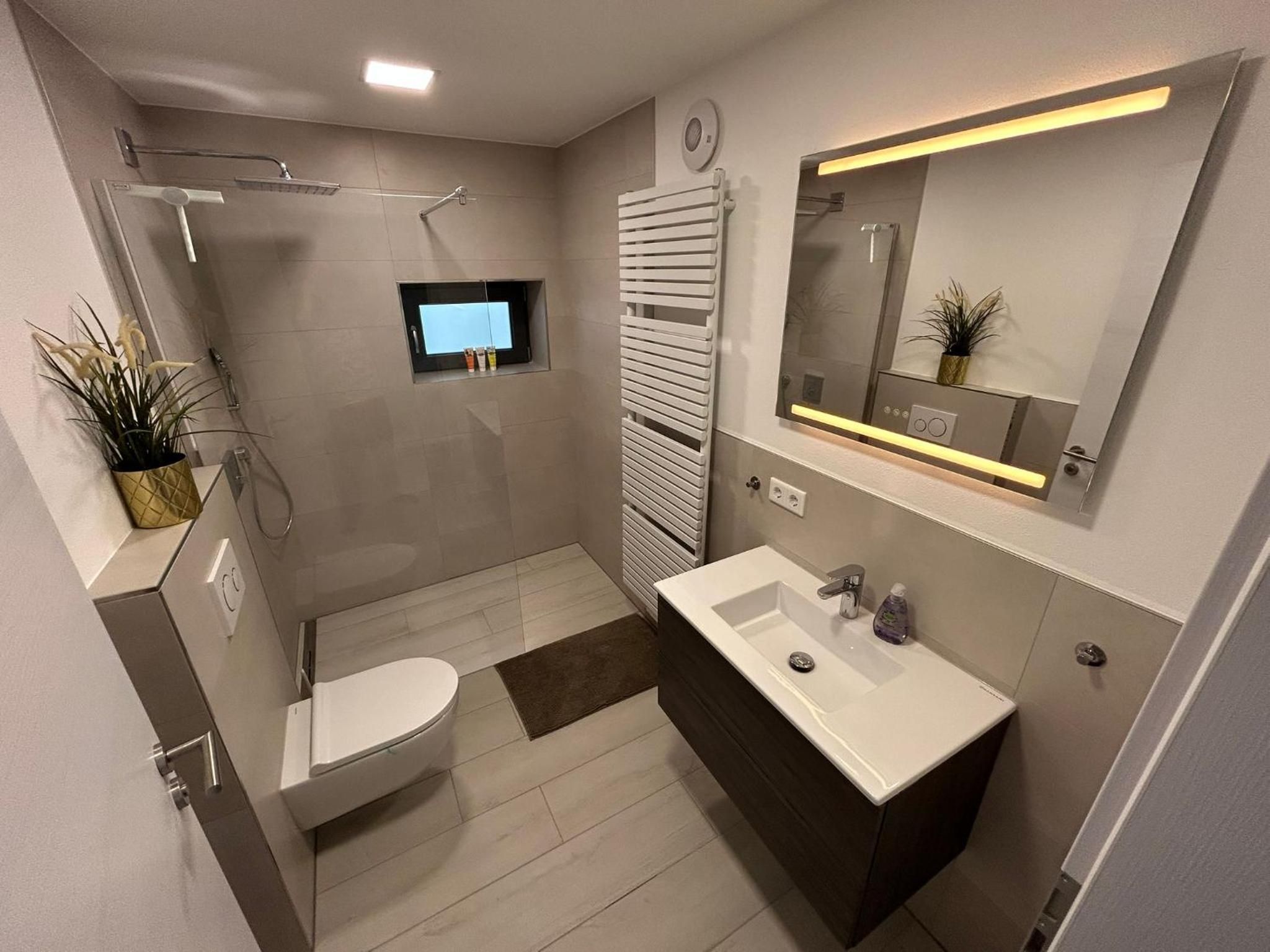 Bad mit bodengleicher Dusche, Waschtisch, WC und beleuchtetem Spiegel