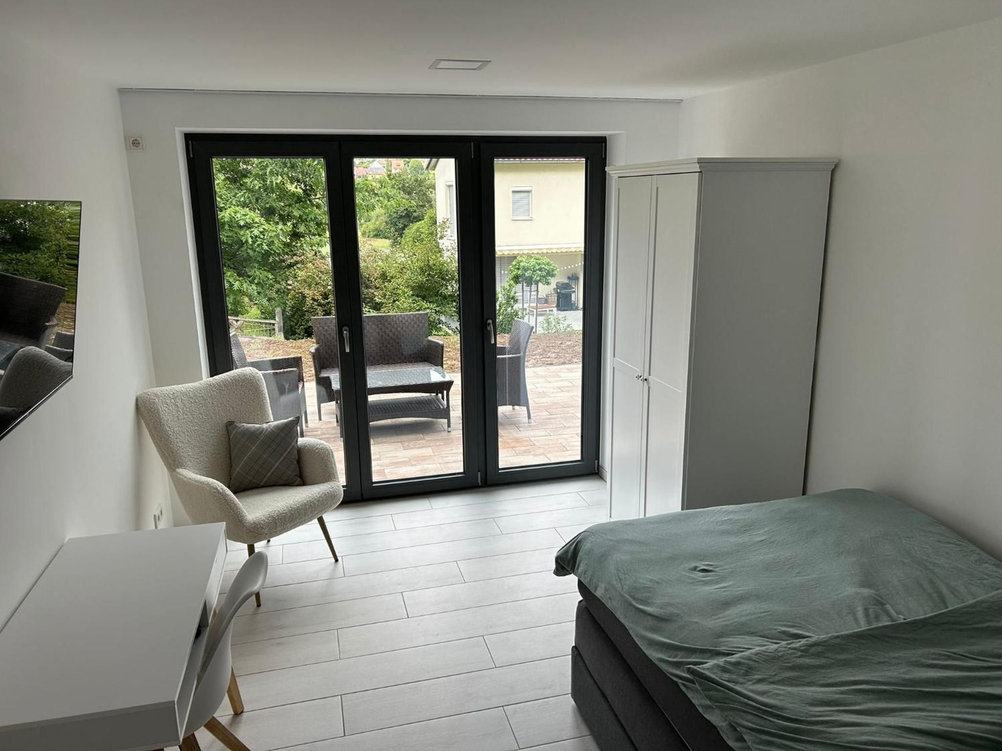 Einzelzimmer: Sessel vor der Terrassentür, rechts Kleiderschrank und Bett, links der Schreibtisch