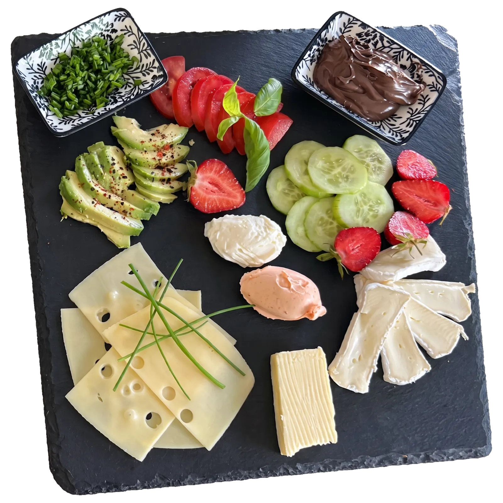 Frühstück auf einer Schieferplatte: Schnittkäse mit Schnittlauch, Camembert, Frischkäse, ein rosa Aufstrich, Butter, Avocado, Tomate mit Basilikum, Gurke, Erdbeeren, dazu je ein Schälchen Schnittlauch und Nutella